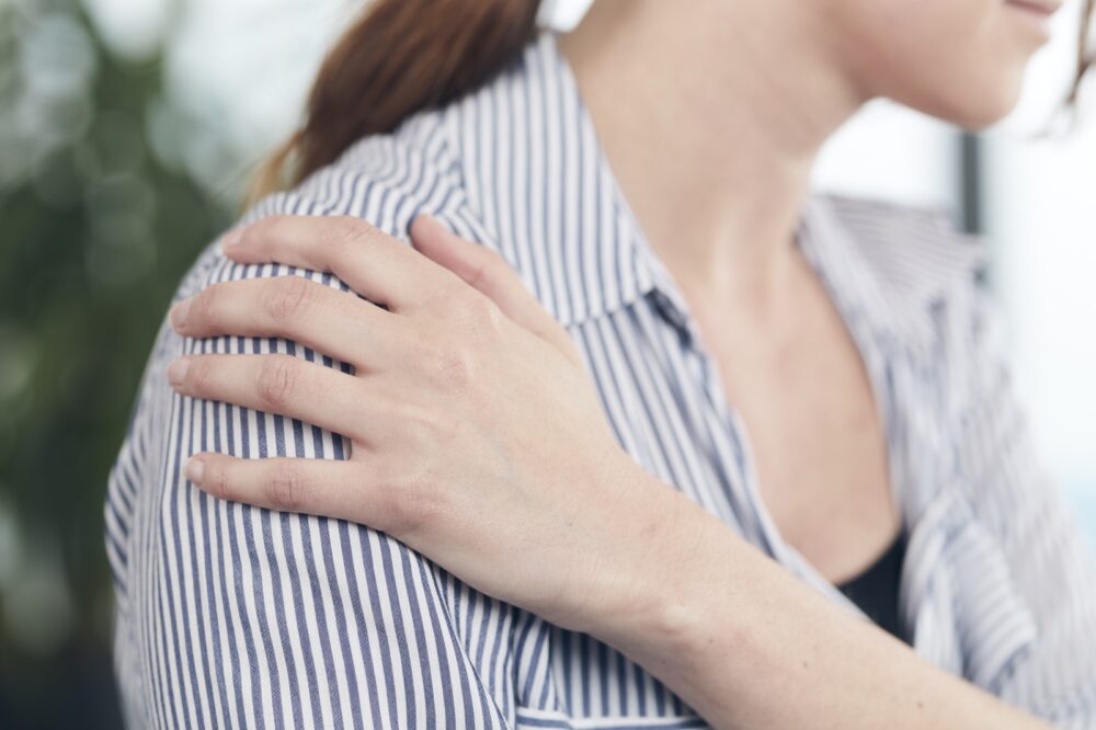 Vrouw houdt de voorkant van haar pijnlijke schouder vast - Spine Clinics