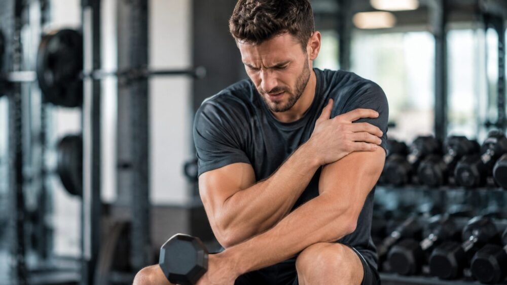 Sporter in de sportschool pakt zijn schouder vast door overbelasting – Spine Clinics